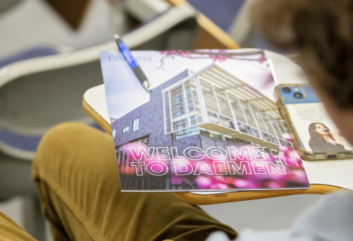 Welcome to Daemen orientation book on a desk a student is sitting at